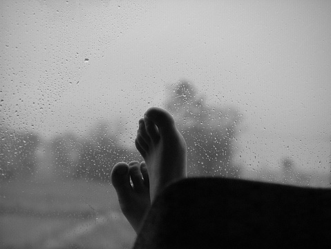 Pies de una chica en una ventana de un autobús mojada por la lluvia en blanco y negro