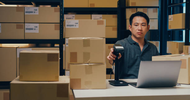 istock Asian businessman use barcode machine scan customer data in paper box and type register online information order detail in laptop for send express delivery at warehouse. 1439502447