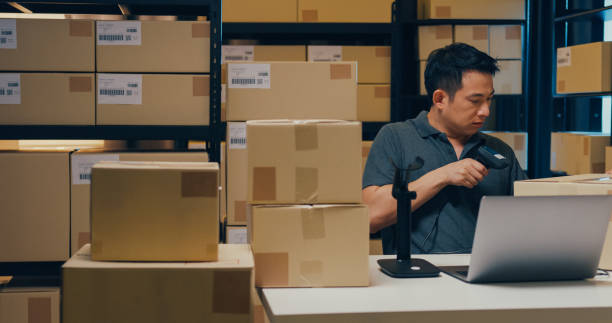 istock Asian businessman use barcode machine scan customer data in paper box and type register online information order detail in laptop for send express delivery at warehouse. 1439502449