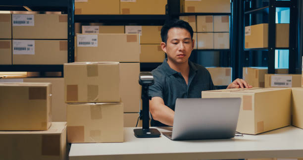 istock Asian businessman use barcode machine scan customer data in paper box and type register online information order detail in laptop for send express delivery at warehouse. 1439502474