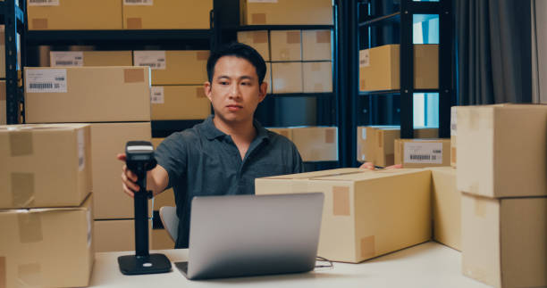 istock Asian businessman use barcode machine scan customer data in paper box and type register online information order detail in laptop for send express delivery at warehouse. 1439502486