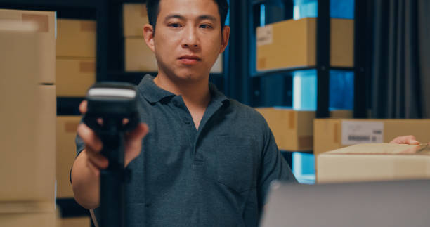 istock Close-up Asian businessman use barcode machine scan customer data in paper box and type register online information order detail in laptop for express delivery at warehouse. 1439502499
