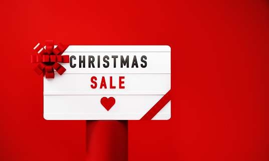 Christmas Sale written white lightbox sitting on red podium before red background. Horizontal composition with copy space.