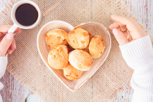 istock Cheese bread (brazilian Pao de Queijo mineiro) and coffee, heart-shaped plate, woman's hand, top view flat lay 1439511999