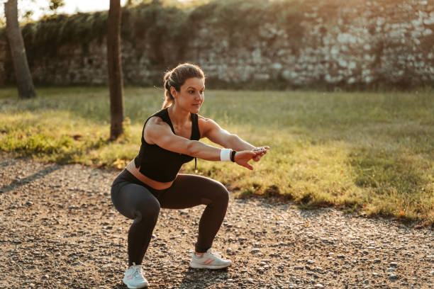 Beautiful young woman exercising in the park, doing squats.