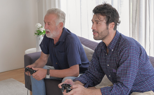 Two of caucasian old father and son family are enjoy to playing game console together in living room sofa on holiday.