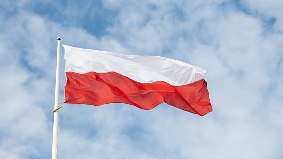 Flag of Poland waving at wind against beautiful blue sky. Polish flag White and red flutters on blue sky. National flag of Poland flapping on flagpole with sky behind