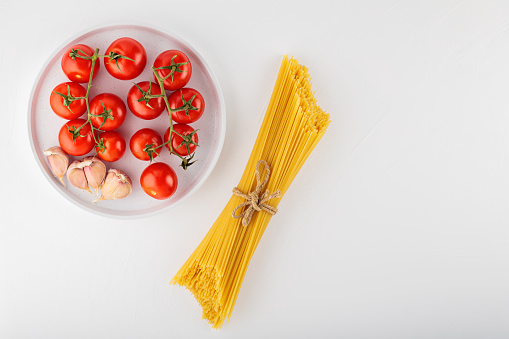 Spaghetti pasta with tomatoes and garlic on white background. Dry italian pasta prepared from durum wheat and vegetables. Top view. Copy space