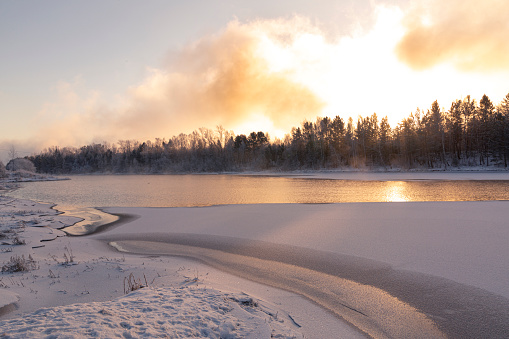 Winter landscape with frozen river on a frosty day. Weather, climate change.