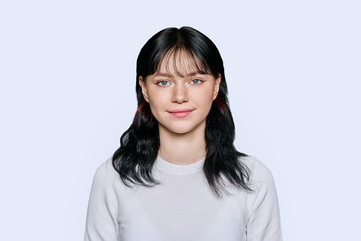 Portrait of happy smiling young female looking at camera on light studio background. Attractive girl student 18, 19 years old posing.