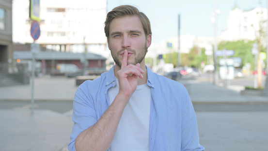 Outdoor Portrait of Man with Finger on Lips, Please be Quiet