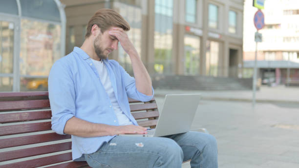 istock Man with Headache Using Laptop while Sitting Outdoor on Bench 1439527837