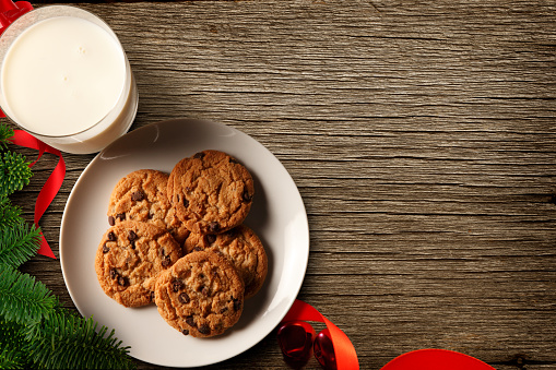 A glass of milk and a plate of cookies wait for Santa Claus on a wood table that provides ample room for copy or text.