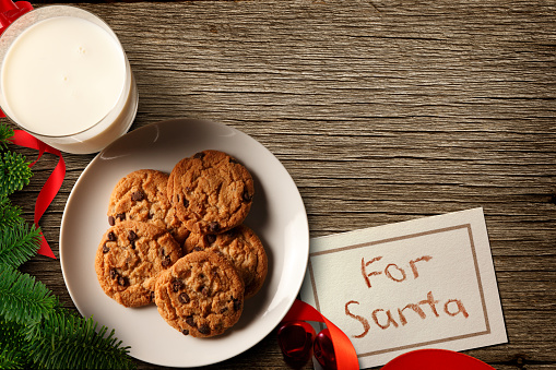 A glass of milk, a plate of cookies, and a childs note wait for Santa Claus on a wood table on Christmas Eve.
