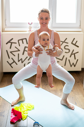 Happy mother exercising whit her baby girl in the bedroom on exercise mat