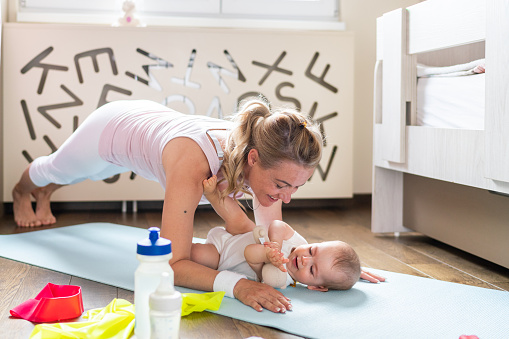 Happy mother exercising whit her baby girl in the bedroom on exercise mat