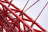 Close-up of fragment of red cable-stayed bridge pylon in place where metal cables are fastened. Close-up shows connection of steel powerful straight crossbar, bridge connection, metal architecture.