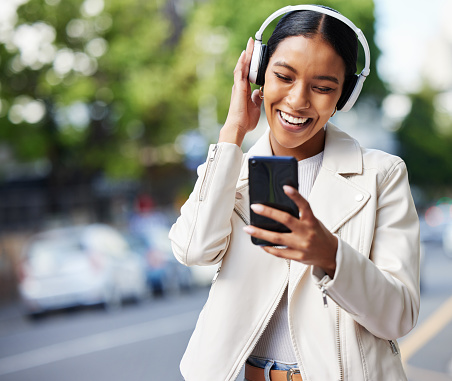 Happy city girl with phone and headphones listening to music, podcast or streaming a online subscription service movie. Black woman watching funny web comedy, internet meme or social media app video