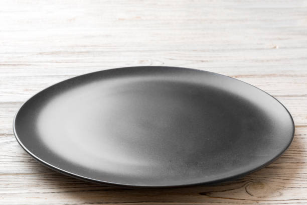 istock Perspective view of empty black plate on wooden background. Empty space for your design 1439537662