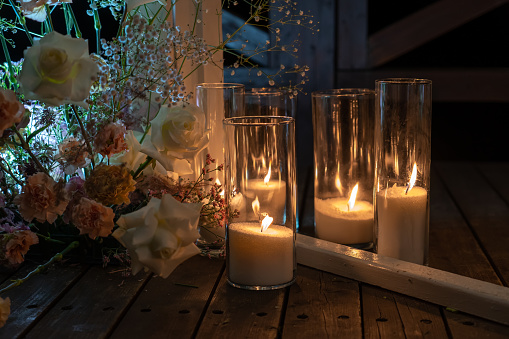 Burning white candles in a glass bulb stand wooden terrace of country hotel decorated with wedding bouquets at romantic evening