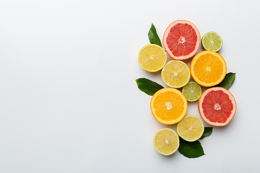 Stock photo showing citrus fruit wedges and slices on mottled grey background, modern minimalist photo of circular sliced oranges, lemon and lime citrus fruits showing segments, seeds / pips and rind around edge, healthy eating concept photo for vitamin C and fruit juice.