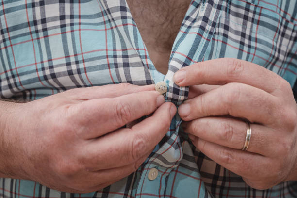 istock Close-up of a man's hands buttoning a plaid shirt. 1439537881