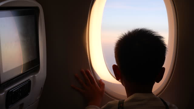 Asian boy look at the airplane window, during sunset