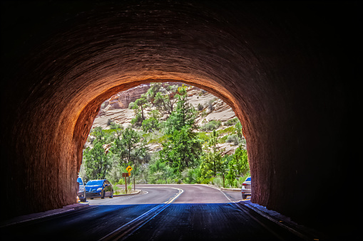 The light at the end of the Tunnel at south end of Zion National Park Showing bright light and trees and cliffs and a few cars parked