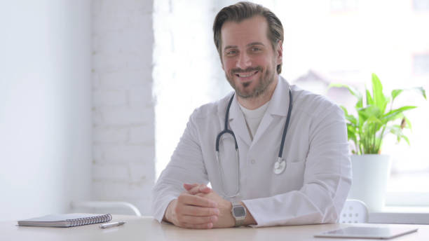 istock Young Doctor Smiling at Camera While sitting in Clinic 1439543996