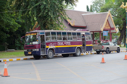 Thai bus at Erawan National Park in Kanchanburi. Bus is parked on parking lot and is connecting par area with city Kanchaburi. In background is a building