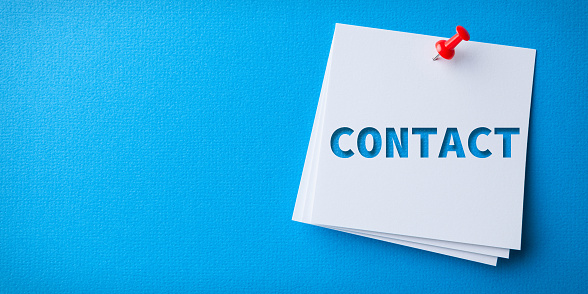 White Sticky Note With Contact Us And Red Push Pin On Blue Background