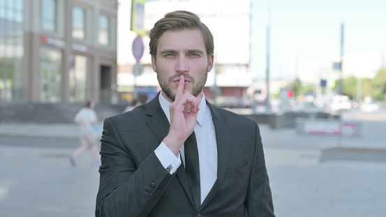 Outdoor Portrait of Businessman with Finger on Lips, Please be Quiet