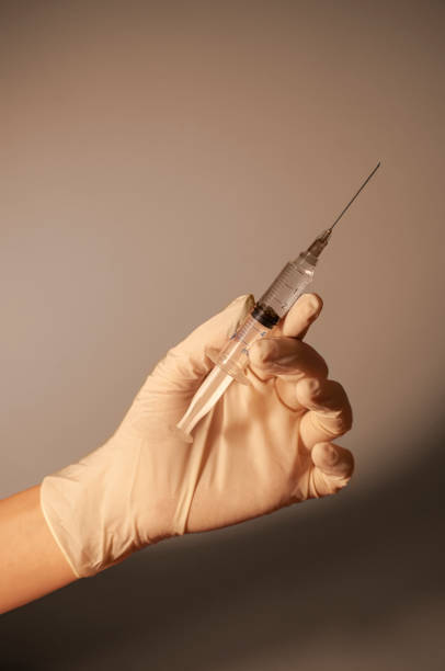 istock Syringe in hand with rubber glove on neutral background. 1439552341