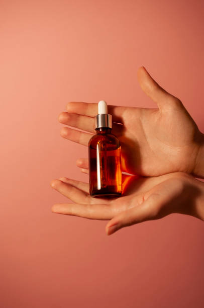istock Brown bottle with serum in hand against a pink background. 1439552348