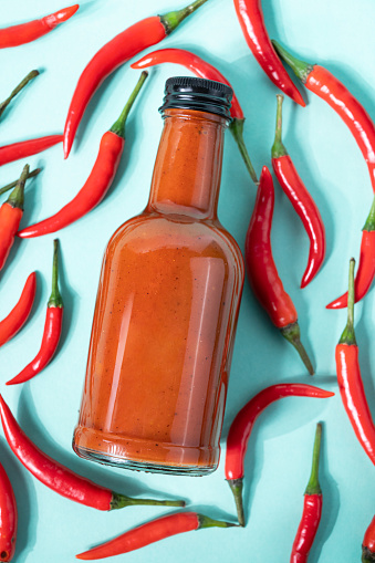 Hot chili sauce in a bottle on a bright blue background with fresh red pepper. The concept of vegetarian delicious food. Top view.