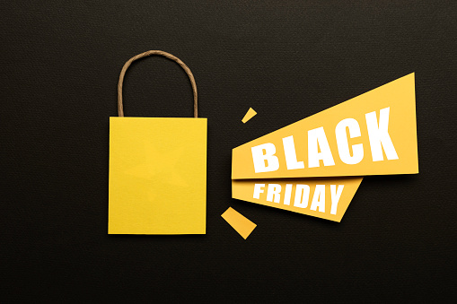 Yellow shopping bag, yellow papers with announcement effect and Black Friday text on it on black background.