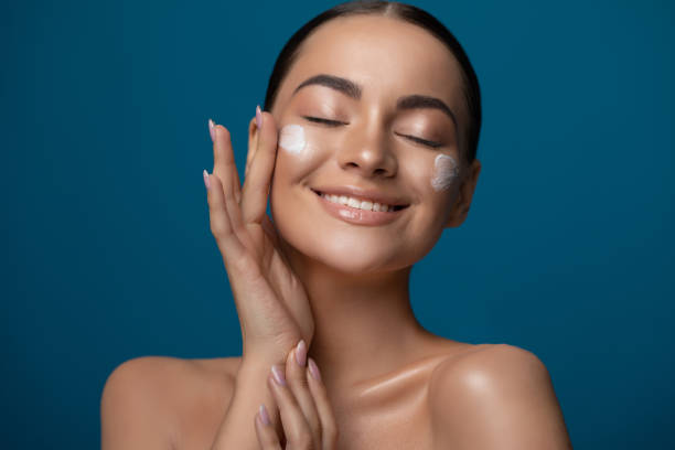 Close up beauty portrait of a beautiful young woman applying face cream stock photo