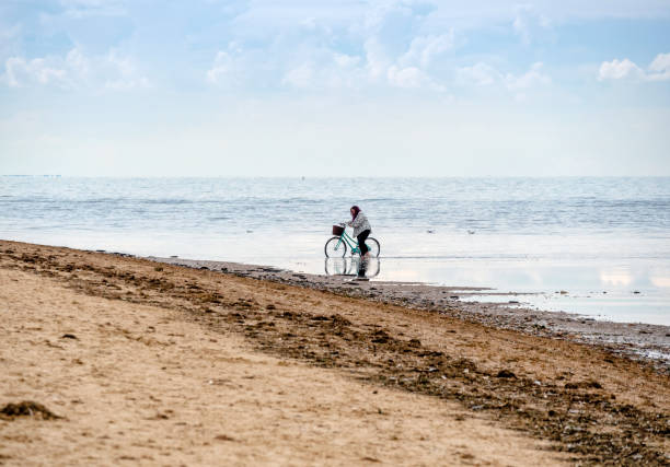 A  woman paddling with her bicycle in the shallow water off the beach at Old Hunstanton, Norfolk, Eastern England.