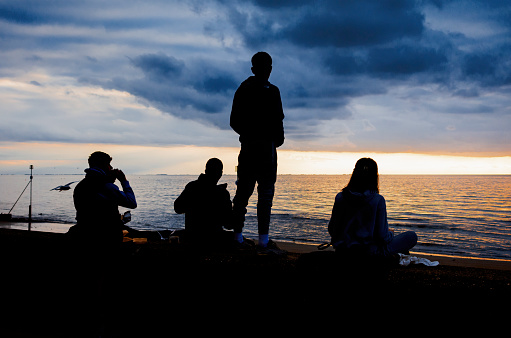 A group of silhouetted young people watching the sunset over The Wash from Hunstanton, Norfolk, Eastern England.