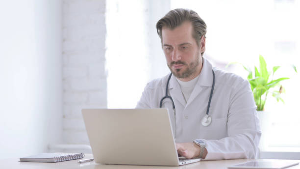 istock Young Doctor Working on Laptop in Clinic 1439560338