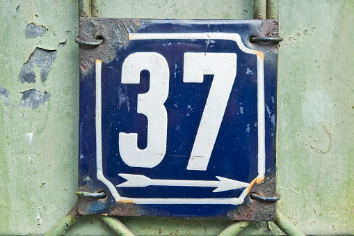 Weathered grunge square metal enameled plate of number of street address with number 37