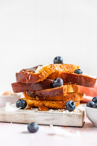 Stack of sweet french toasts with berries, caramel sauce and coconut flakes on pink background. Homemade brioche.