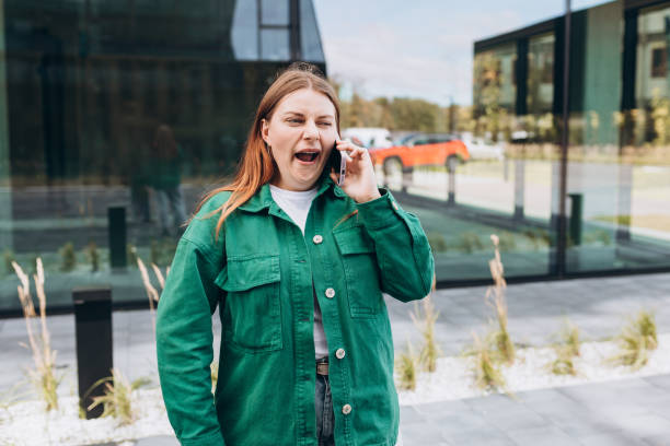 belle femme rousse ennuyée parlant avec son smartphone. femme bâillant et utilisant un smartphone dans la rue de la ville. - rudeness blah customer boredom photos et images de collection