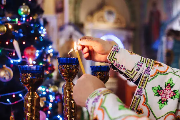 Photo of Close-up of a priest lighting candles in a church. Christmas service in the Ukrainian Orthodox Church.