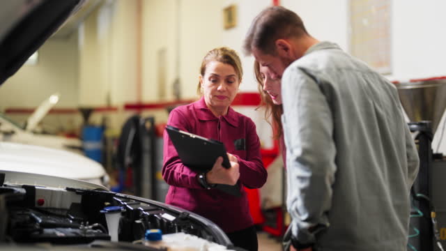 Car mechanic expert checking broken car and discussing with couple