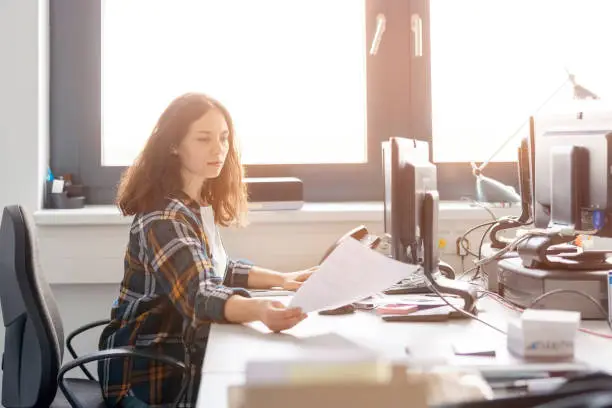 Woman sitting at desk looking at documents while working distribution warehouse office. Young woman working at import export warehouse office.