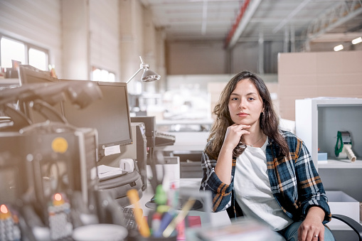 Portrait of confident young woman working at warehouse office. Young woman sitting at her desk at distribution warehouse staring at camera.