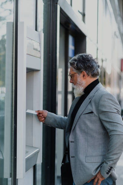 istock Senior business man using atm machine and credit or debit card 1439569511