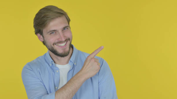 istock Young Man Pointing on Side on Yellow Background 1439570380