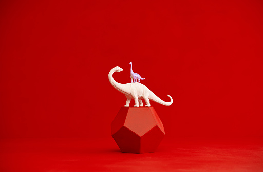 Pair of dinosaurs on a red plinth with  red background and copy space
